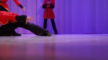 Tanınmayan çocuklar Kazak dansı yapıyor. Sahnede bir grup dansçının performansı. Kostümlü adamlar sahnede coşkuyla zıplıyorlar. Yüksek kalite 4k görüntü
