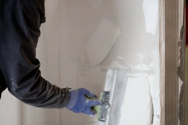 İşçiler duvara bir spatula ile macun uzatıyorlar. Daire tadilatı. Alçıpan arasında kapılar açılıyor. Kopyalayacak yer de var. Yüksek kalite fotoğraf