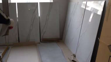 Bir adam büyük formatlı bir fayansı bir çizime göre karşılaştırır. Döşeme üzerindeki desenlerin seçimi ve ayarlanması. 120 'ye 60 fayans döşeme hazırlığı. Yüksek kalite 4k görüntü