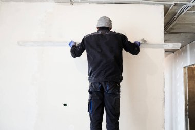 Bir inşaat işçisi, bir yenileme projesi kapsamında kusursuz bir son elde etmek için ustalıkla yüzeyi düzleştiren bir kuralla beton duvarı kaplıyor. Yüksek kalite fotoğraf