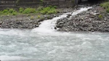 Mzymta Nehri 'nin setin etrafındaki taşlardan oluşan bir setin arka planına karşı hareketi. Nehir hızlı akan bir akıntıyla akar. Yüksek kalite 4k görüntü