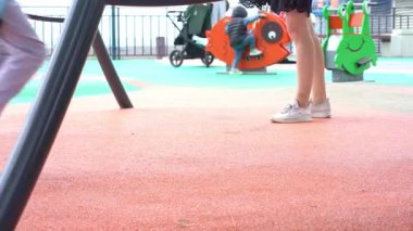 Oyun parkında salıncakta sallanan bir çocuğun yan görüntüsü. İkinci salıncakta bir kadın küçük bir çocuğu sallıyor. Bölgedeki kauçuk yüzey. Yüksek kalite 4k görüntü