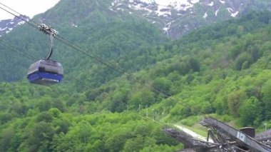 Mekanizması olan bir teleferik. Bulutlar ve açık gökyüzü arasında karla kaplı dağların resimli görüntüsü. Kablolu araba ve açık havada ağaçlık bir alanın arka planında asansörler. Yüksek kalite 4k görüntü