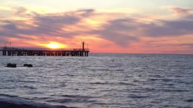 Dalgalı deniz manzarası ve ahşap iskele. Deniz manzarası göz kamaştırıcı bir gün batımı. Güzel alacakaranlık gökyüzü ve beyaz bulutlar. Rahatlamak için harika bir plaj arka planı. Yüksek kalite 4k görüntü