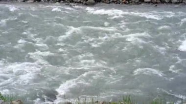 Dalgalar ve dalgalarla su yüzeyinin detaylı yakın görüntüsü. Vahşi dağ nehri, set boyunca akan temiz dere, dinamik çekim. Yüksek kalite 4k görüntü