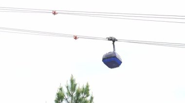 Gökyüzünün arka planındaki teleferiğin füniküleri ağaçların arkasına gidiyor. Beyaz bulutlu gökyüzü manzaralı kablolar. Yaz ya da sonbahar mevsimi. Yüksek kalite 4k görüntü