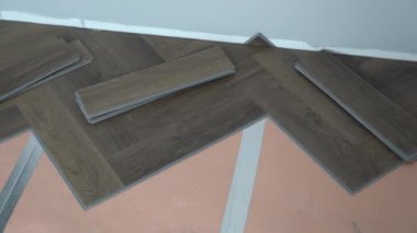 Tanınmayan bir kişi, bir apartman veya evin yenilenmesi sırasında döşeme işlemini gösterir. Laminat veya kuvars vinil kaplama koyu renk ve ahşap desenli. Yüksek kalite 4k görüntü