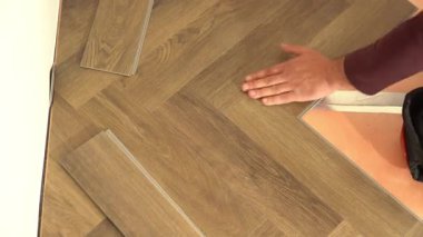 Bir işçi, bir apartman dairesinde veya evde tadilat sırasında kuvars vinil döşeme döşemesi serer. Laminat veya kuvars vinil kaplama koyu renk ve ahşap desenli. Yüksek kalite 4k görüntü