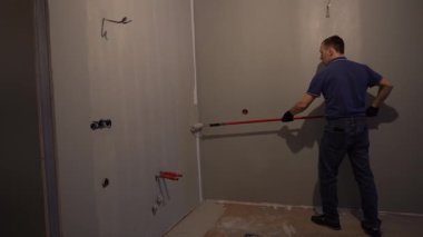 Bir adam boya silindiriyle duvar boyuyor. Daire boyası, gri boyalı yenileme. Daire tadilatı. Yüksek kalite 4k görüntü