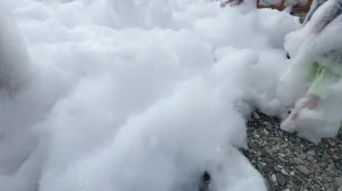 Çocukların ayakları sahilde köpükle koşuyor. Köpük partisi için beyaz köpük. Plaj köpük veya köpük tabakasıyla kaplı. Tatilde yapılan bir tatil. Yüksek kalite 4K görüntü.