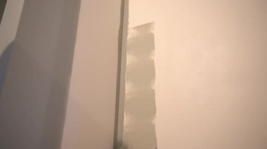 Mükemmel bir duvar resmi için bir adam boya rulosuyla duvar boyuyor. Tepeden tırnağa patinaj hareketi. Yüzeyde gri boya var. Yüksek kalite 4k görüntü