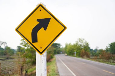 Doğru eğri üzerinde bir uyarı işareti olan ve arka plan kavramı olarak bir yolu olan veya çeşitli reklamlar için kullanılabilen bir trafik tabelası.