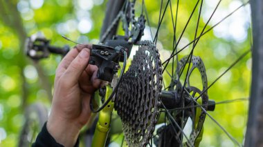 Yeşil arka planda bir bisikletçi çıplak elleriyle şanzımanı tamir ediyor.