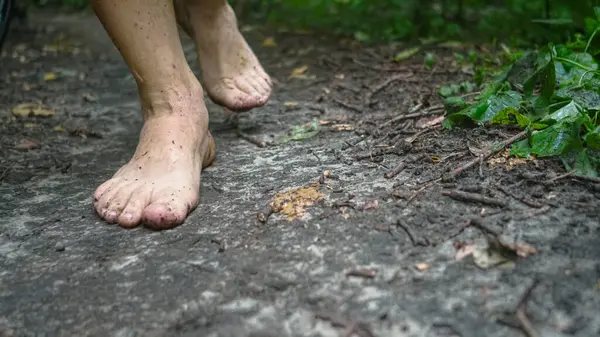 man walks in nature with bare feet, forest path and grass