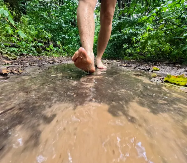 a man with bare feet walks along a forest path after the rain