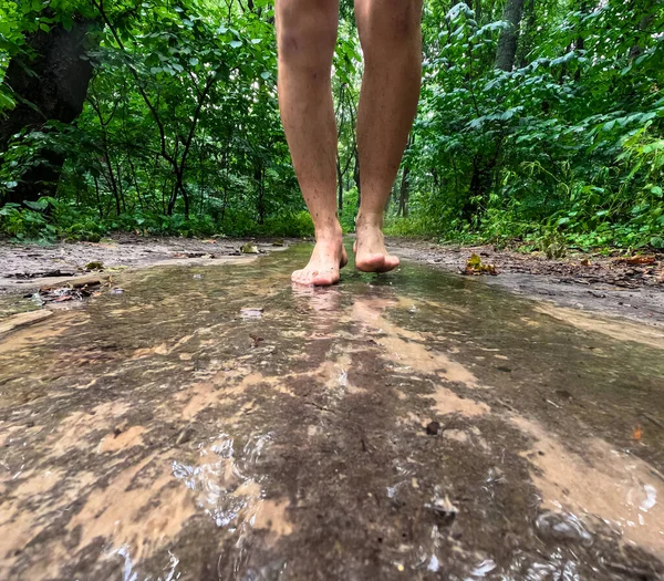 a man with bare feet walks along a forest path after the rain