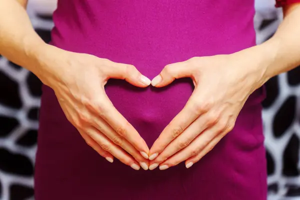 Woman hands made a heart on her stomach. Waiting for a child. The concept of pregnancy, motherhood, preparation and expectation.