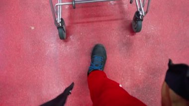 Süpermarketteki erkek müşterinin ayakları, yakın çekim, alışveriş alanında alışveriş arabası yuvarlanan adam. Seçici odak