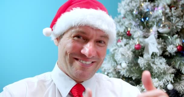 クリスマスの帽子の幸せなお父さんクリスマスツリーの背景にあるサンタクロースは クラスの親指を見せ お父さんの幸せな顔 幸せな男の顔休日に喜び — ストック動画