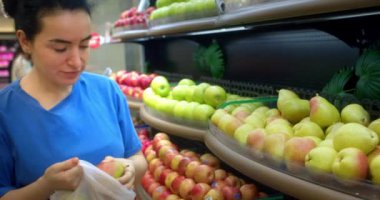 Kadın olgun armutları raftan alır ve bir sepete koyar. Çekici genç kadın marketten taze armut sebzesi seçiyor. Market kavramı.