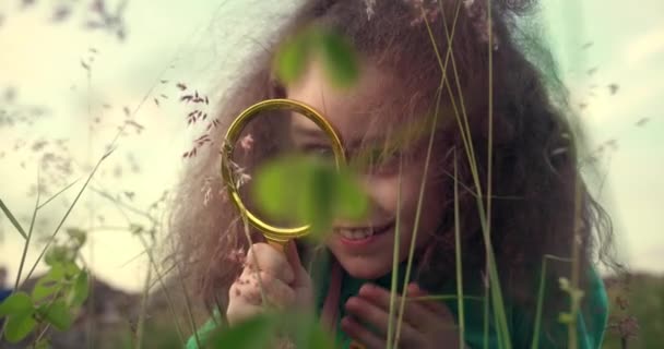 幸せな小さな笑顔の女の子は自然界で虫眼鏡を通して見ています 子供は公園の芝生で夢を見る 幸せなかわいい赤ちゃん 赤ちゃんの笑顔とカメラを見てください — ストック動画