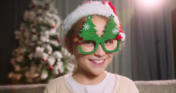 크리스마스 크리스마스 안경을 어린이의 소파에 장식된 크리스마스 카메라를 미소짓고 소녀의 — 비디오