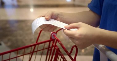Kadın alışveriş merkezinden alışveriş yaptıktan sonra alışveriş arabasındaki Sevgili Miktar faturasını kontrol ediyor. Gıda fiyatlarında artış, hipermarkette para harcamak. Kadın market arabasını kontrol ediyor..