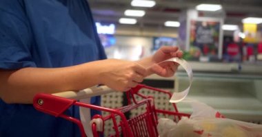 Gıda fiyatlarında artış, hipermarkette para harcama. Kadın market arabasını kontrol ediyor. Kadın alışveriş merkezinden alışveriş yaptıktan sonra bakkal arabasındaki Sevgili Miktar faturasını kontrol ediyor.