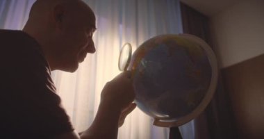 Odaklanmış iş adamı girişimci evde oturuyor güneş ışığında odada dünyaya bakıyor, büyüteçle dünyayı keşfediyor.