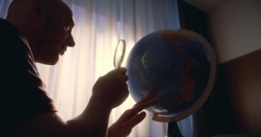 Odaklanmış iş adamı girişimci, sabah gün batımında evde oturur, dünyaya bakar, büyüteçle dünyayı keşfeder. Küre kullanan adam evde oturup, dünyada doğru ülkeyi arar.