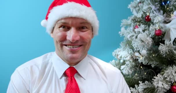 クリスマスの笑顔大人の男Vloggerサンタの帽子はカメラトークを見て コンピュータアプリの記録ブログVlogを使用してオンラインチャットライブビデオ会議コールを作るバックグラウンドで自宅でクリスマスツリー ウェブカメラ — ストック動画