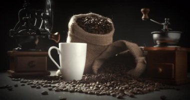 Adam kahve çekirdeklerini öğütüp öğütüyor. Sıcak kahve fincanı ve bir avuç kahve çekirdeği. 4K arka planında espresso öğütücüleri olan dumanı tüten bir bardak.