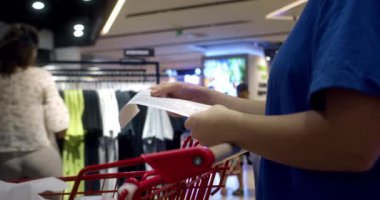 Kadın alışveriş merkezinden alışveriş yaptıktan sonra alışveriş arabasındaki Sevgili Miktar faturasını kontrol ediyor. Gıda fiyatlarında artış, hipermarkette para harcamak. Kadın market arabasını kontrol ediyor..