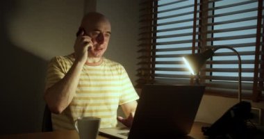 Professiona denen adam gece geç saatlere kadar çalışıyor. Telefonda konuşuyor. Ofisteki bilgisayarda çalışırken uzaktan kumandalı iş sorunlarını çözüyor. Gülümseyen adam aktif olarak dizüstü bilgisayarın başında otururken konuşuyor.