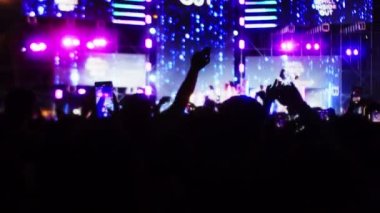 Siluet hayranları sahnede parlak flaş ışıkları önünde ellerini kaldırıyor, kafalarında ışık olan kızlar, konserde eğleniyorlar. Kalabalık dans ediyor.