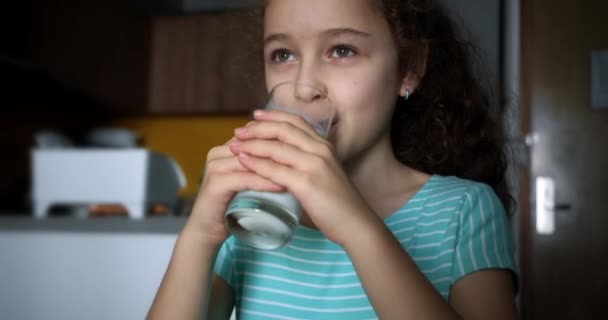 テレビを見ながら自宅のソファに座っている間に女の子の肯定的な子はミルクを飲みます 朝食の子供の夢の概念を持つ健康的な食品の子供 娘でリビングルームにザソファドリンクヨーグルトミルク — ストック動画