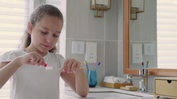 这孩子在牙刷上涂了白牙膏 站在浴室里 在镜子前刷牙 微笑的生活方式 — 图库视频影像