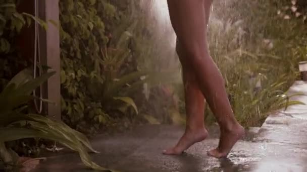 水着姿の女性の背景には 雨のシャワー 背景に熱帯緑を取ります 少女は近代的なオープンバスルームで彼女の頭と体を洗う スローモーション — ストック動画