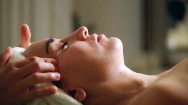 Genç ve çekici esmer kadın güzellik salonunda yüz masajı yaptırıyor. Sağlıklı yaşam tarzı ve vücut bakımı kavramı. Yavaş çekim, yakın çekim.