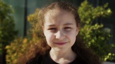 Güneş ışınlarındaki mutlu çocuk. Park 'ın yakın plan portresindeki küçük kız yüzü. Rüya gören komik kız. Güneşin altında bir çocuğun mutlu yüzü. Çocuk kameraya gülümser. Yüzü. Parkta mutlu bir çocuk. Güzel bir yüz. 4K
