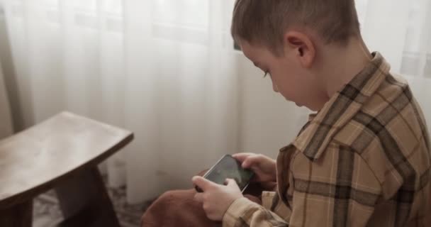 漂亮的6岁男孩在家里用智能手机玩手机游戏 可爱的小男孩在玩手机 孩子在用电话玩游戏儿童在室内玩电子游戏 — 图库视频影像