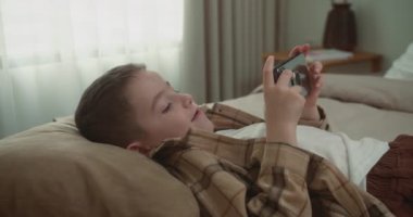 Güzel çocuk. 6 yaşında. Evde akıllı telefondan oyun oynuyor. Cep telefonu çalan sevimli çocuk. Çocuk oyun oynamak için telefonu kullanıyor. İçeride video oyunu oynayan çocuk.