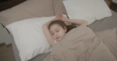 Mavi pijamalı, mutlu, neşeli, küçük bir kızın portresi sabah yatağında uyanır. Çocuk ailesine gülümserken bakıyor, esneyerek gülüyor ve battaniyenin altına saklanıyor..