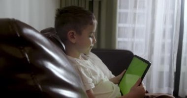 Kanepede tek başına oturan, dijital tablet teknolojisi kullanan meraklı anaokulu çocuğu. Çocuklar teknoloji bağımlılığı konsepti. Home4K 'de küçük çocuk tutucu bilgisayar sörfü internet oyun oyunu.
