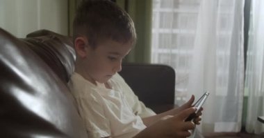Kanepede tek başına oturan, dijital tablet teknolojisi kullanan meraklı anaokulu çocuğu. Çocuklar teknoloji bağımlılığı konsepti. Home4K 'de küçük çocuk tutucu bilgisayar sörfü internet oyun oyunu.
