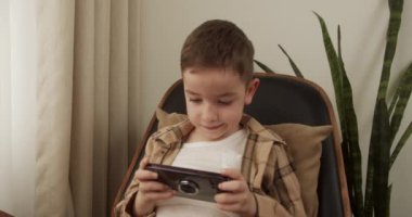 Güzel çocuk. 6 yaşında. Evde akıllı telefondan oyun oynuyor. Cep telefonu çalan sevimli çocuk. Çocuk oyun oynamak için telefonu kullanıyor. İçeride video oyunu oynayan çocuk.