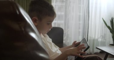Kanepede tek başına oturan, dijital tablet teknolojisi kullanan meraklı anaokulu çocuğu. Çocuklar teknoloji bağımlılığı konsepti. Home4K 'de küçük çocuk tutucu bilgisayar sörfü internet oyun oyunu.
