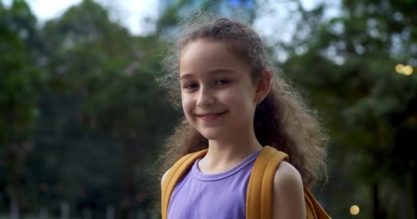 幸せな女子高生 笑顔の女子高生 バックパック付きの小さな女の子の肖像画 単独で日当たりの良い通りの屋外に立って かなり顔小学校5年生4 — ストック動画