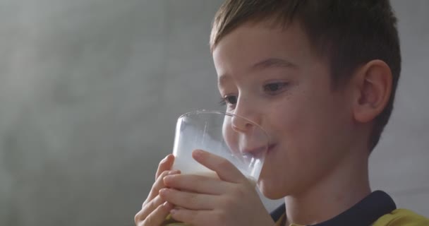 幸せな笑顔の子供はミルクを飲みます 健康的な子供は朝食を食べる子供の夢の概念を食べます キッチンで小さな男の子はヨーグルトミルクを飲み 彼女の唇をなめる — ストック動画