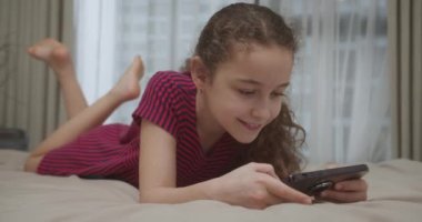 Evde video oyunu oynayan bir çocuk. Güzel bir kız çocuğu. 10 yaşında. Evde akıllı telefondan oyun oynuyor. Cep telefonu çalan sevimli çocuk. Çocuk oyun oynamak için telefonu kullanıyor. 4K.